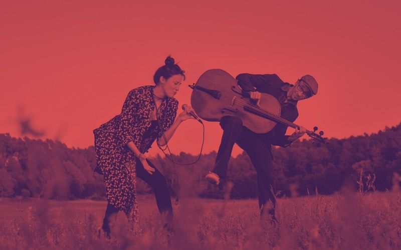 Nihan Devecioglu i Sasha Agranov tocant i cantant a un paisatge rural.
